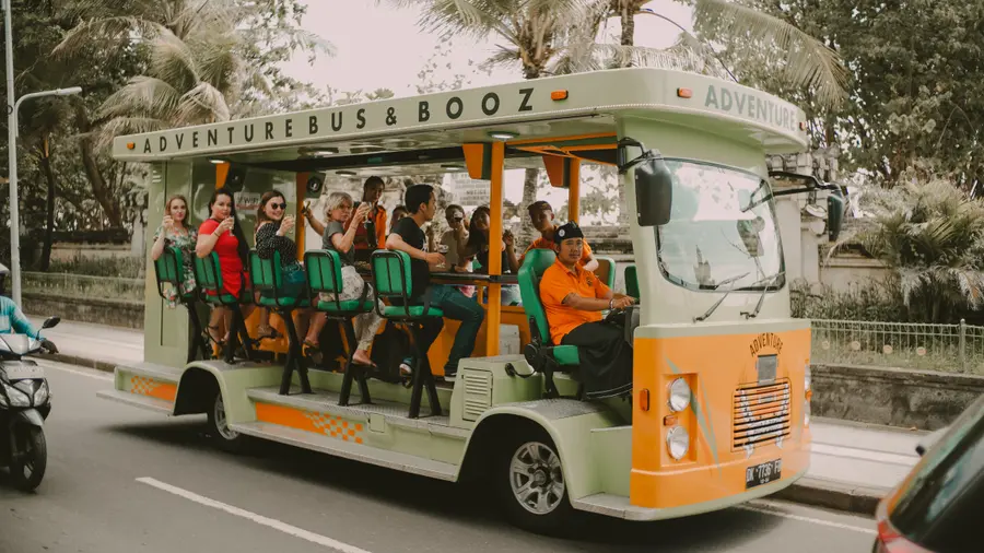 Full side view of the bus cruising a palm-lined Bali road, guests waving