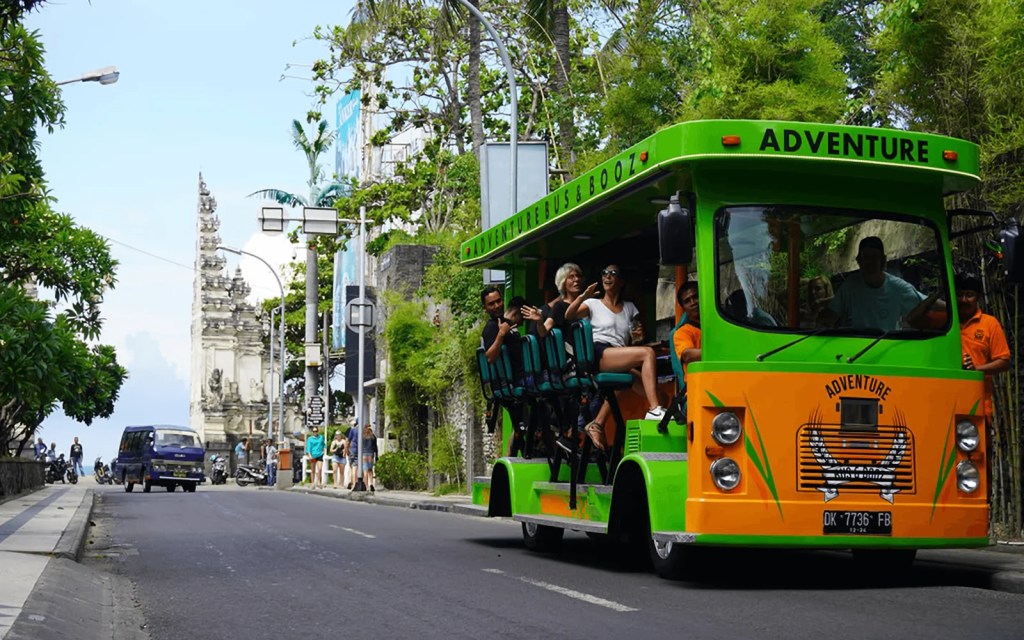 The Bus and Booz party bus arriving past a Balinese temple gate with guests waving